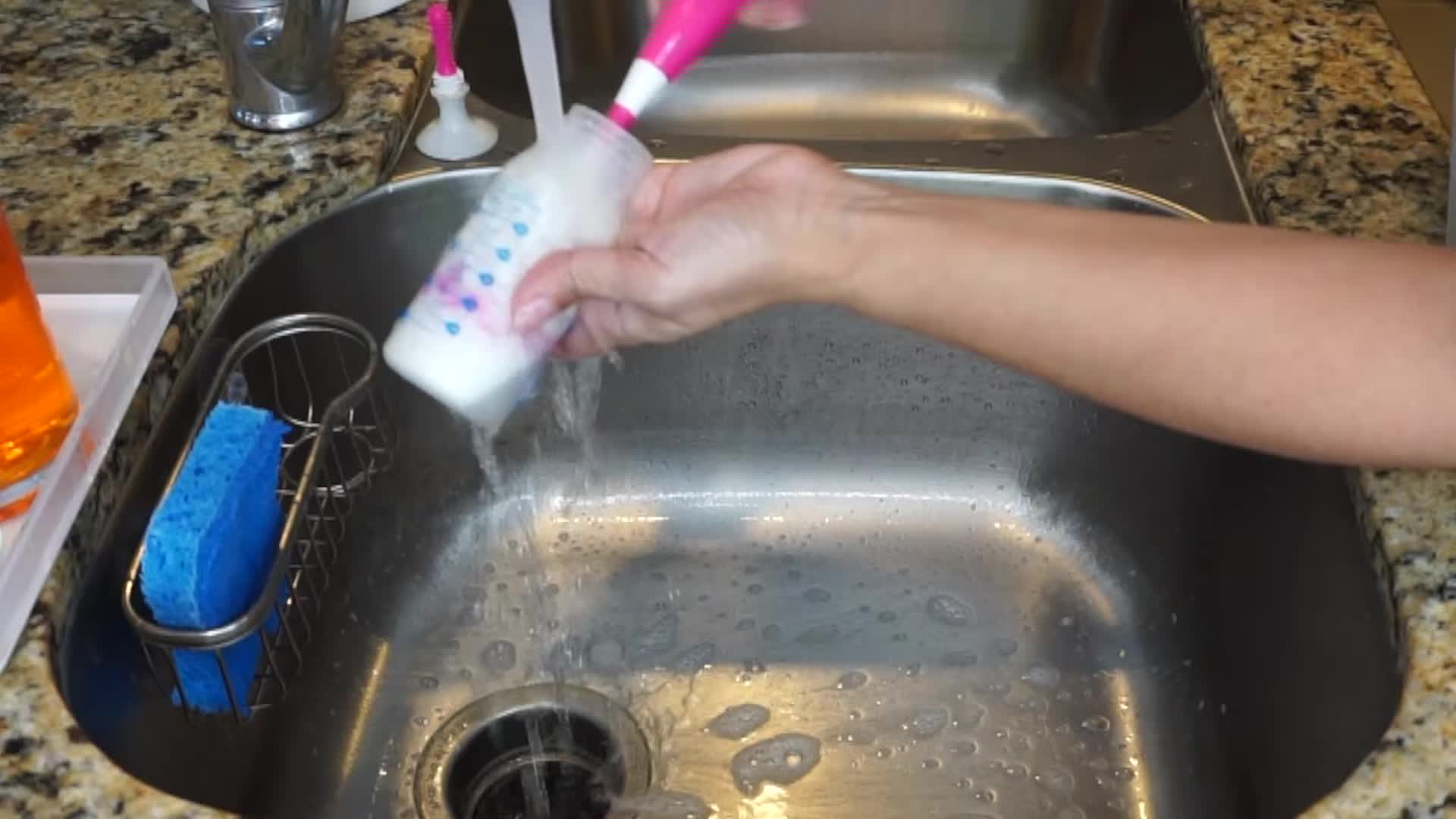 Close-up shot of hands washing a baby bottle with soap and water.